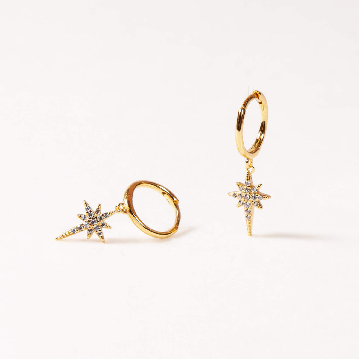 Gold star-shaped earrings and ring on a white background