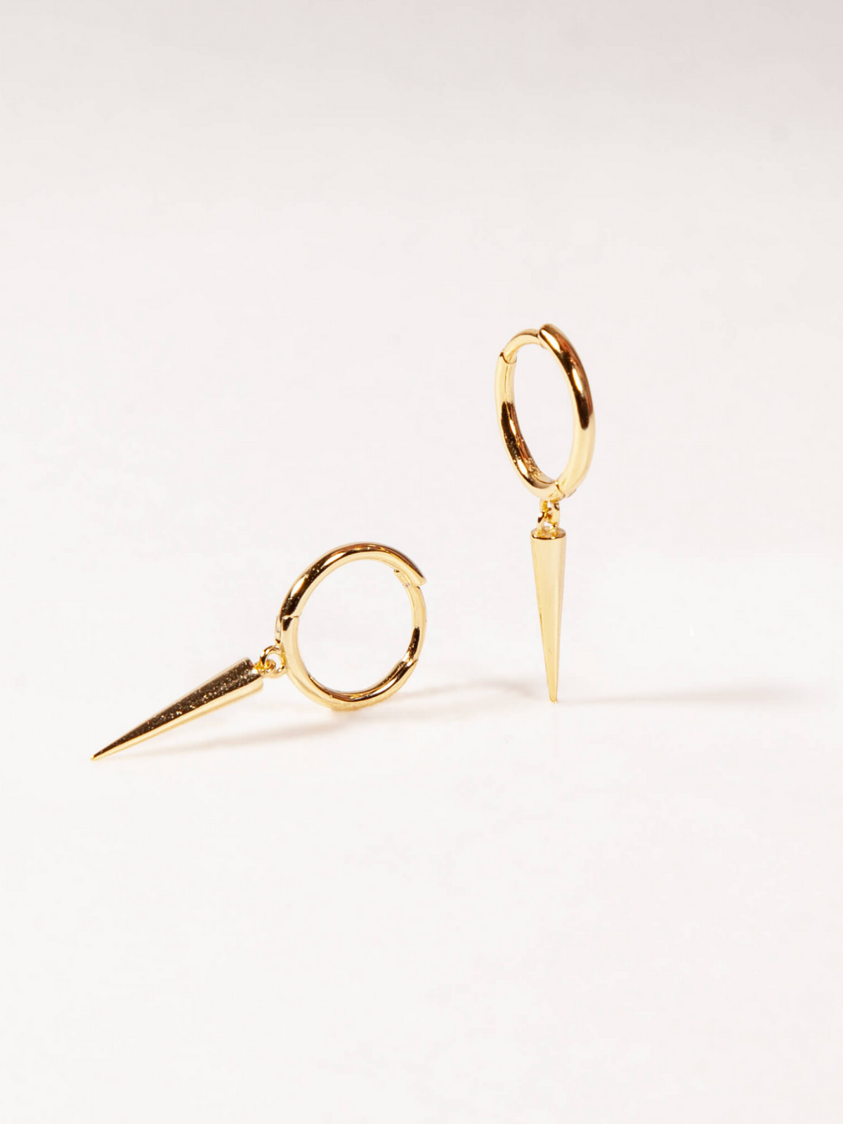 Pair of gold huggies with bar dangle earrings on a light gray background