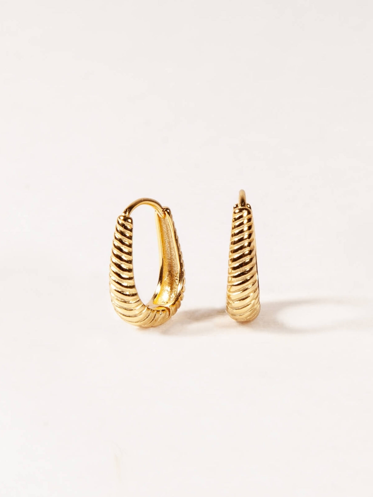 Pair of gold oval hoop earrings on a light beige background