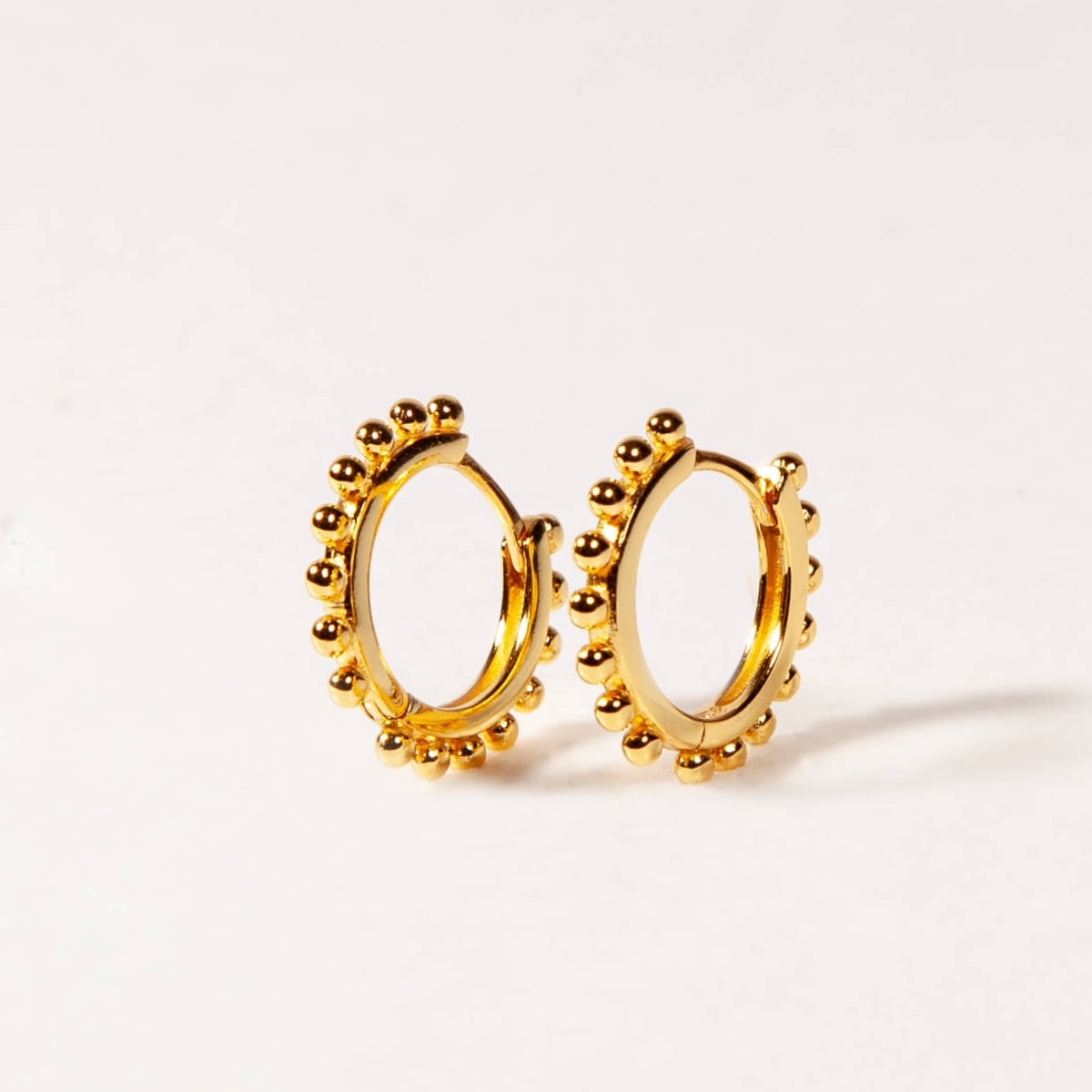 Gold hoop earrings with bead detailing on a light gray background