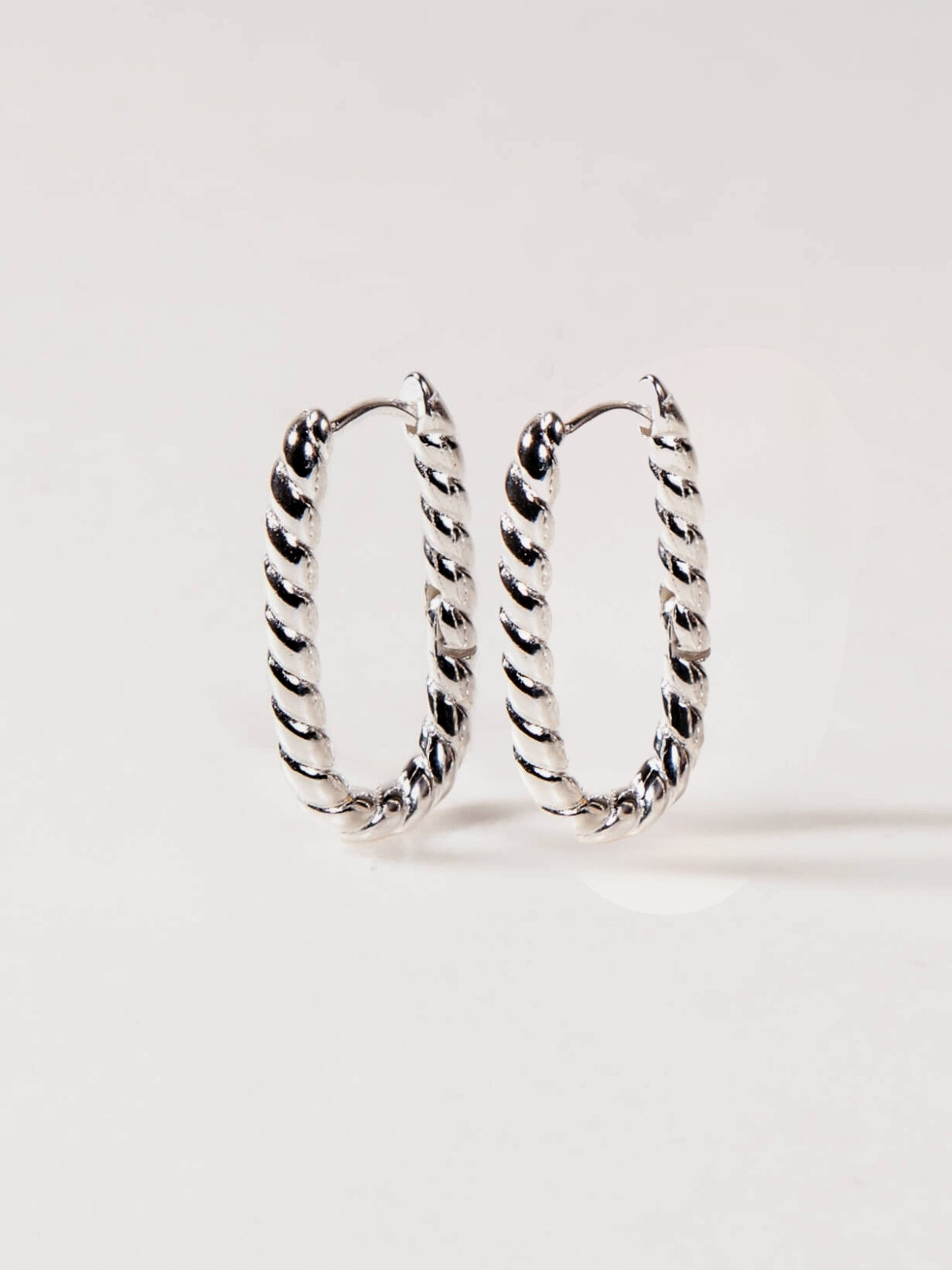 Pair of silver twisted U hoop earrings on a white background