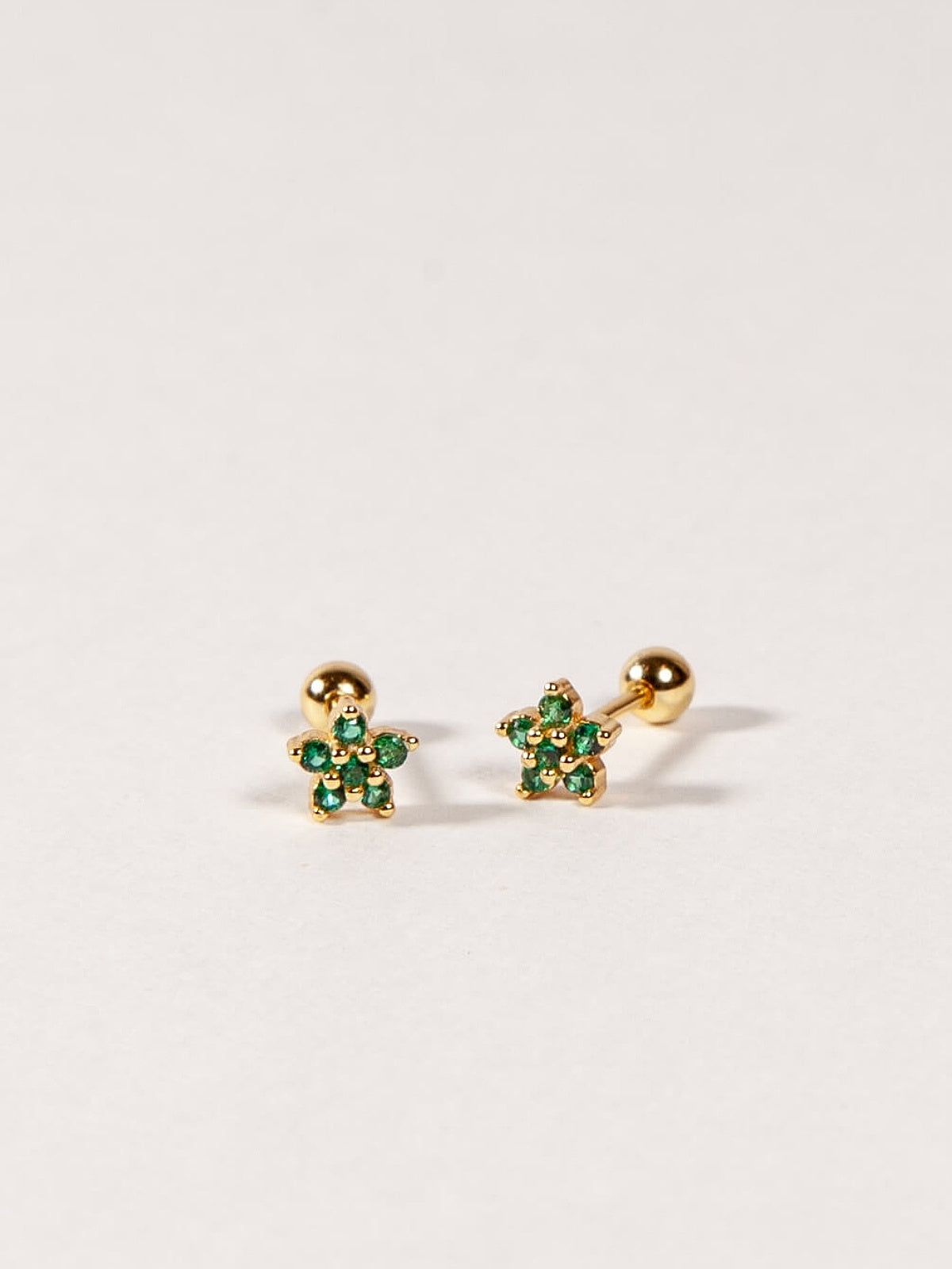 Pair of gold flower-shaped earrings with emerald green CZ stones on a white background