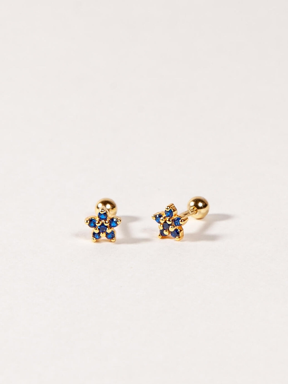 Pair of gold flower-shaped earrings with sapphire blue gemstones on a white background