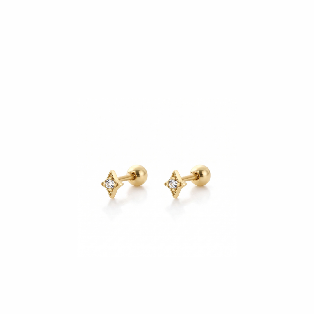 A pair of gold stud earrings with a four-pointed star design, one featuring a small clear gemstone and the other plain, set against a clean white background.