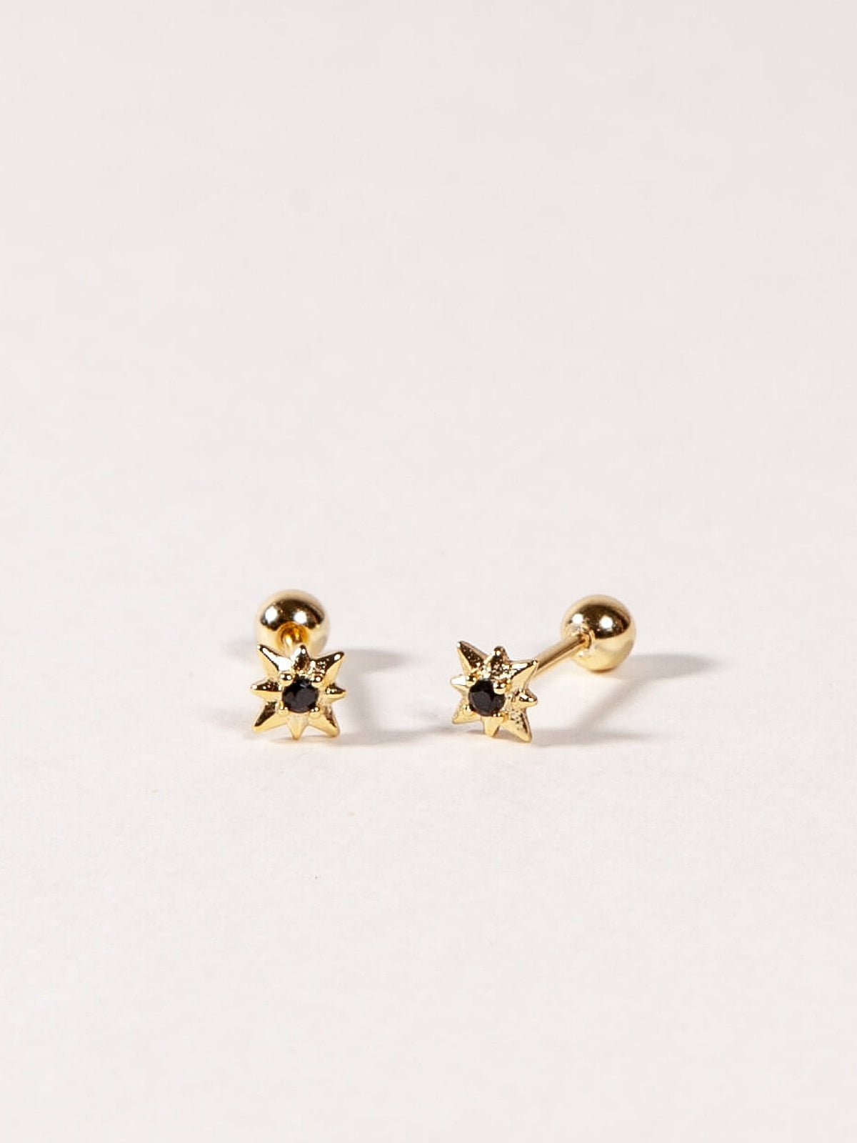 Pair of gold star shape earrings with black CZ Stones on a light gray background