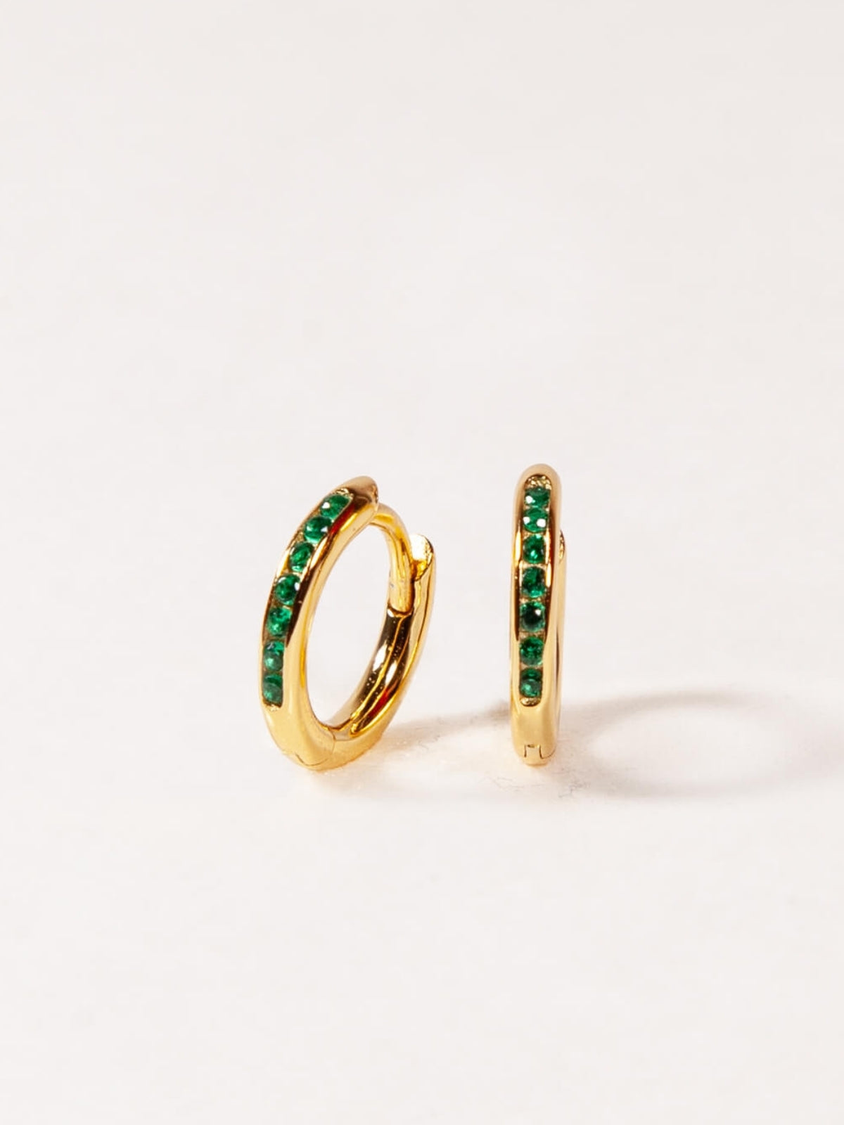 Gold hoop earrings with green gemstones on a white background