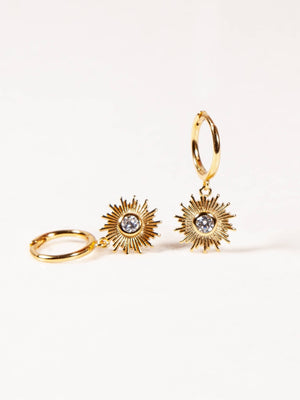 Gold hoop earrings with sunburst designs and clear gemstones on a white background