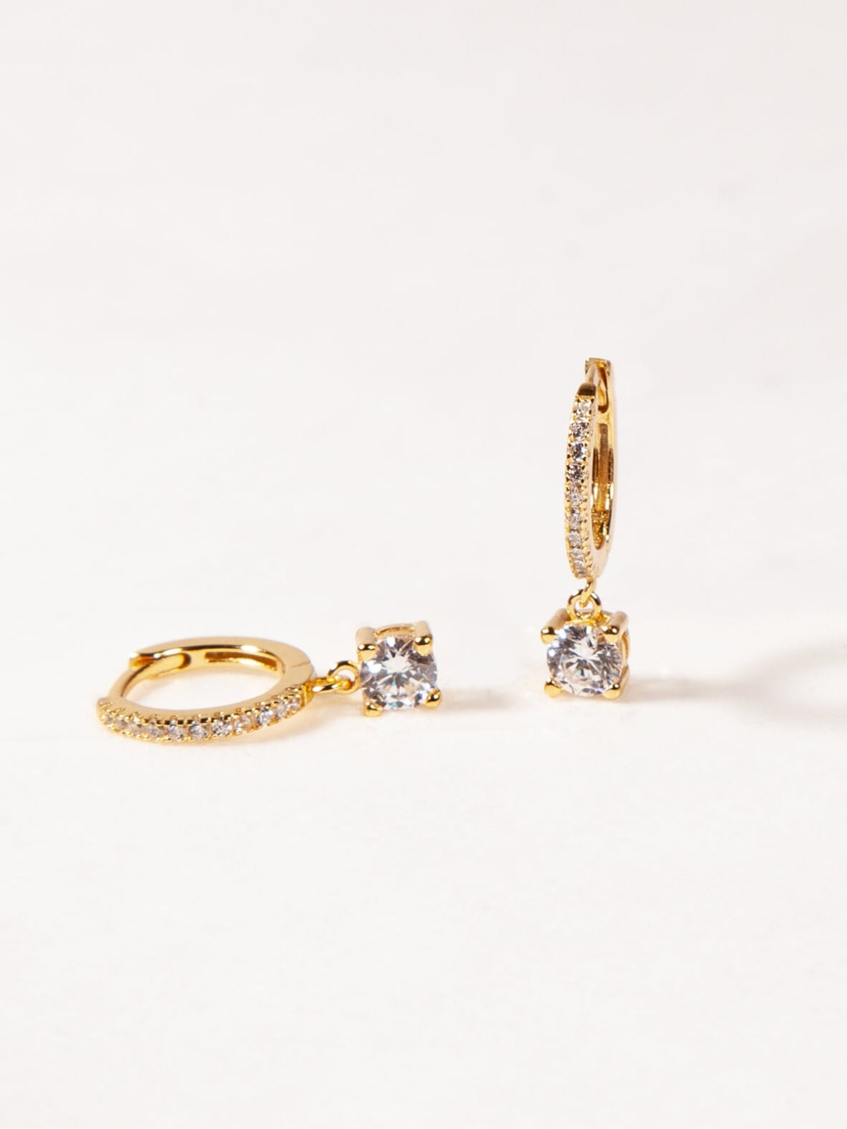 Gold hoop earrings with clear gemstones on a light beige background