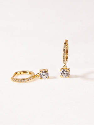 Gold hoop earrings with clear gemstones on a light beige background