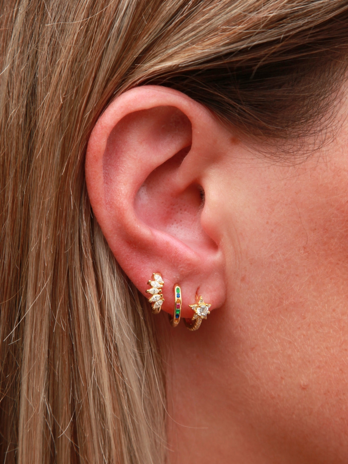 Close-up of an ear wearing a gold earring with gemstones.