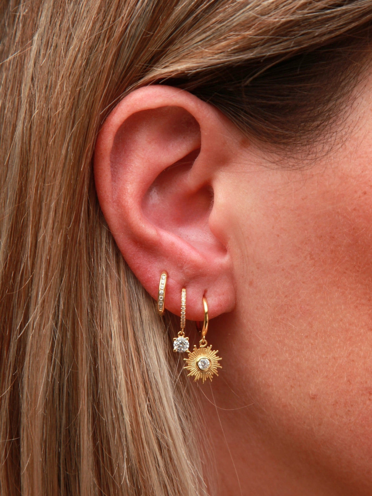 Close-up of an ear wearing gold hoop earrings with small gemstones.