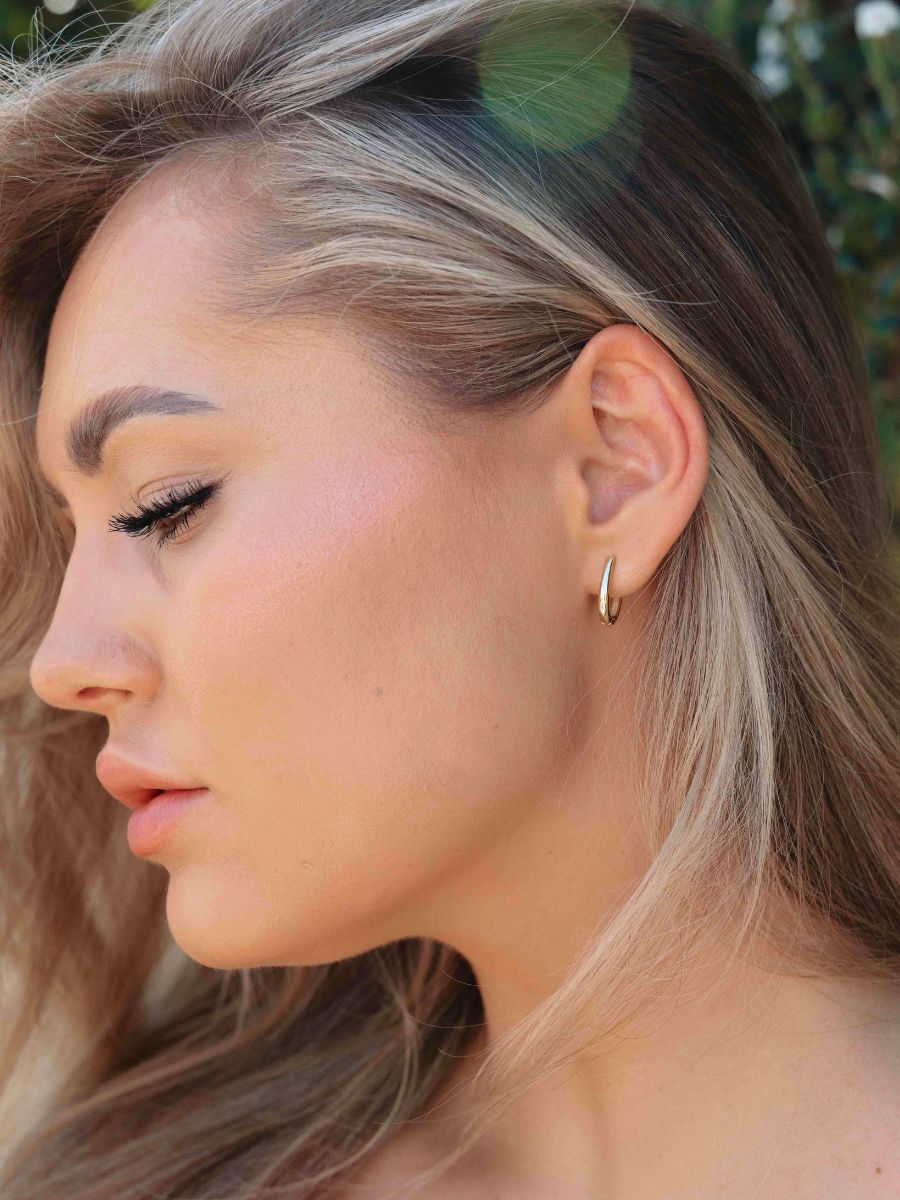 Close-up of an ear wearing gold oval hoop earrings 