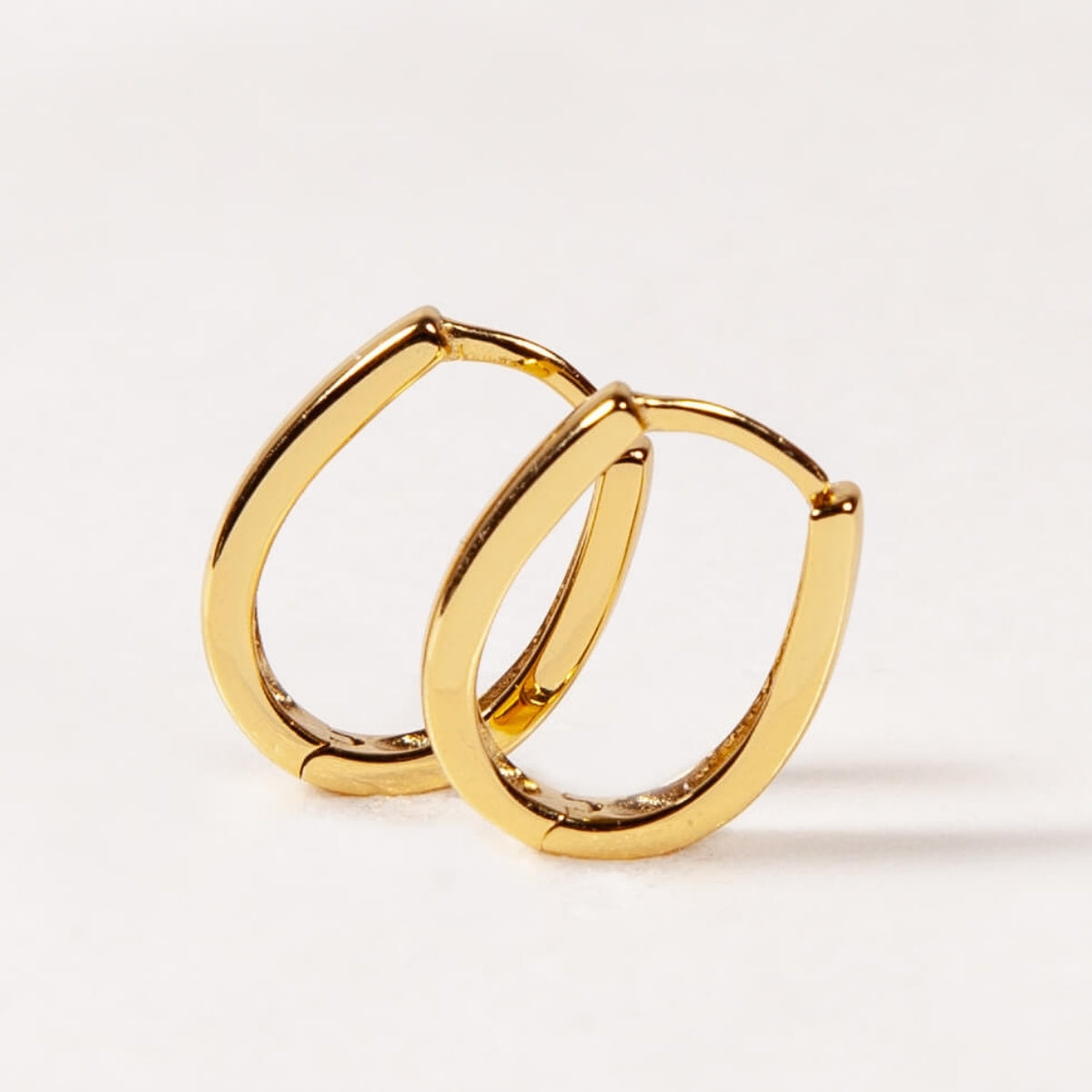 Gold oval hoop earrings on a light beige background