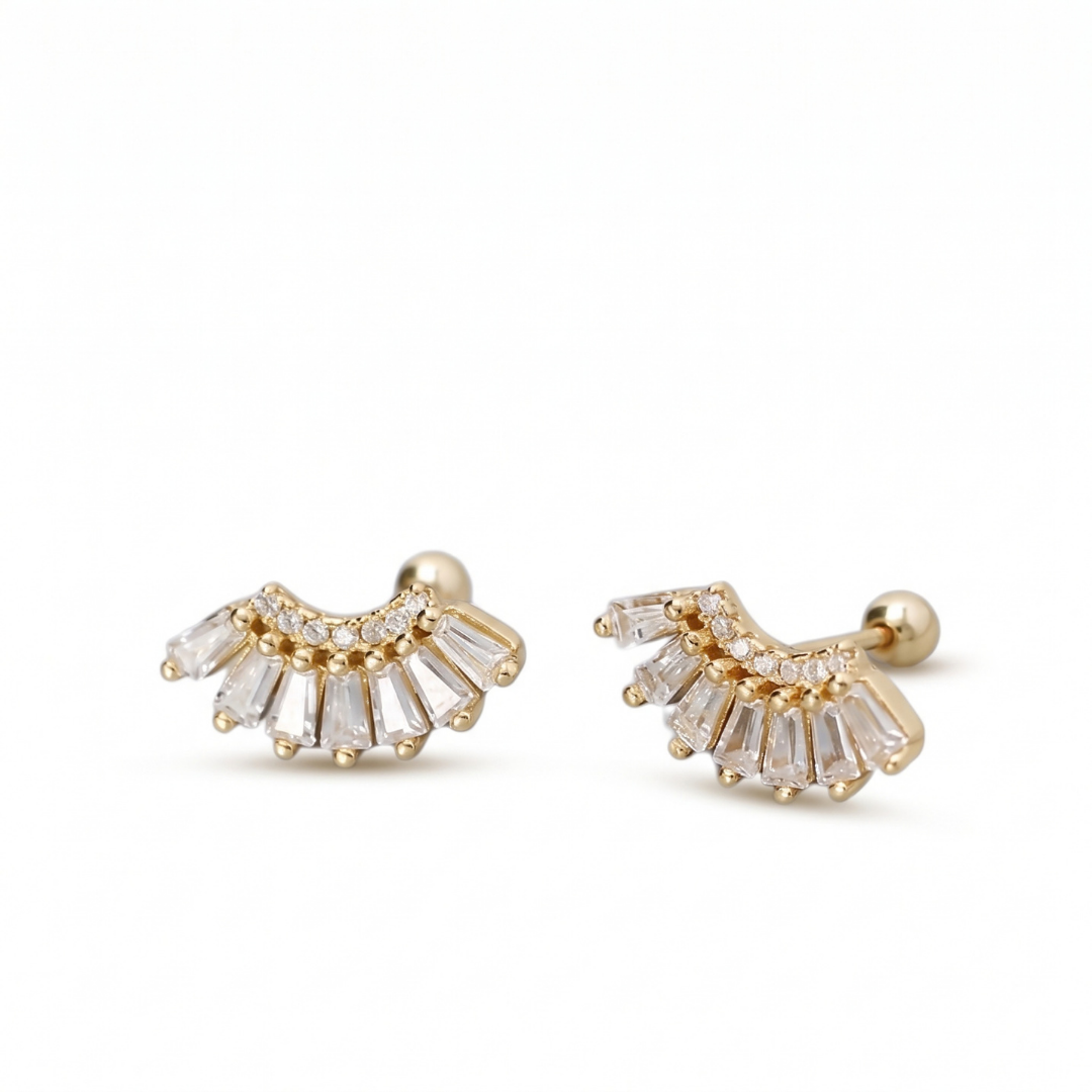 A pair of gold crescent-shaped stud earrings with clear baguette and round crystals, displayed on a clean white background.