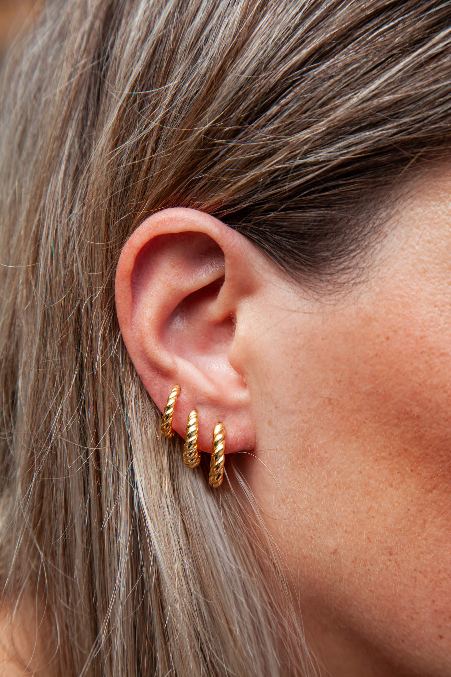 A woman's ear with three twisted hoop earrings