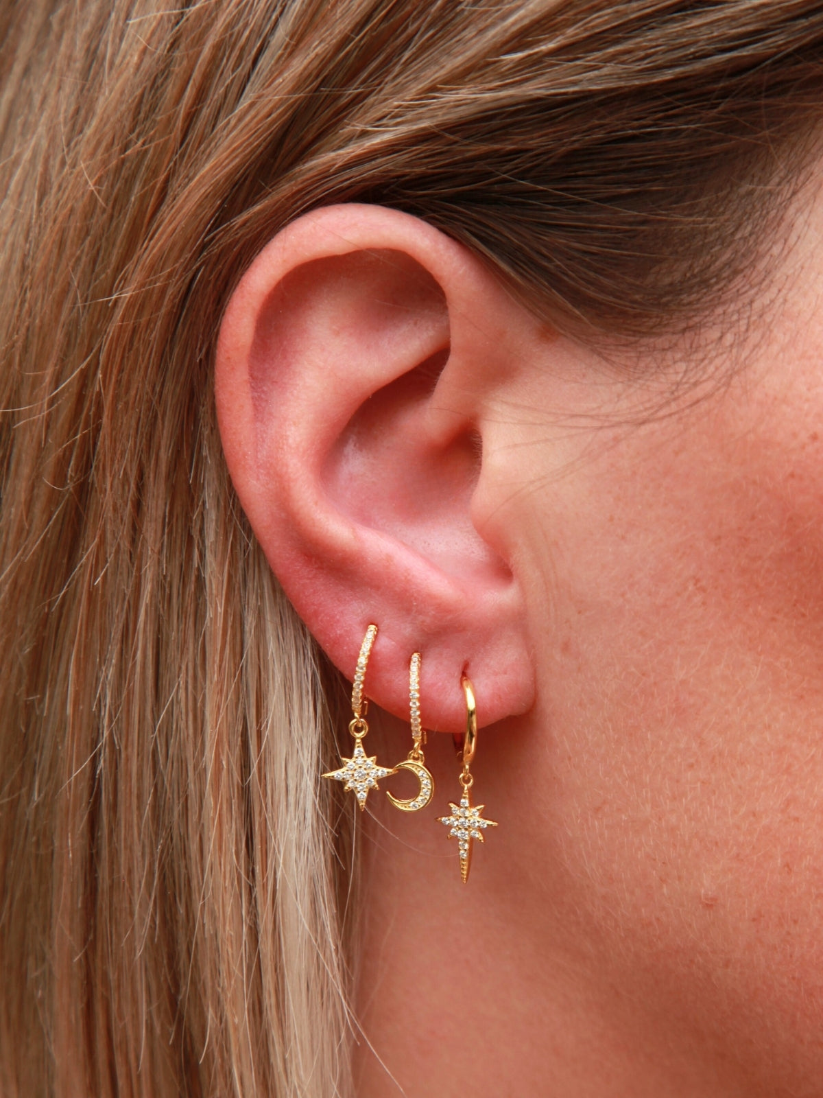 Close-up of an ear wearing gold earrings with star and moon designs.