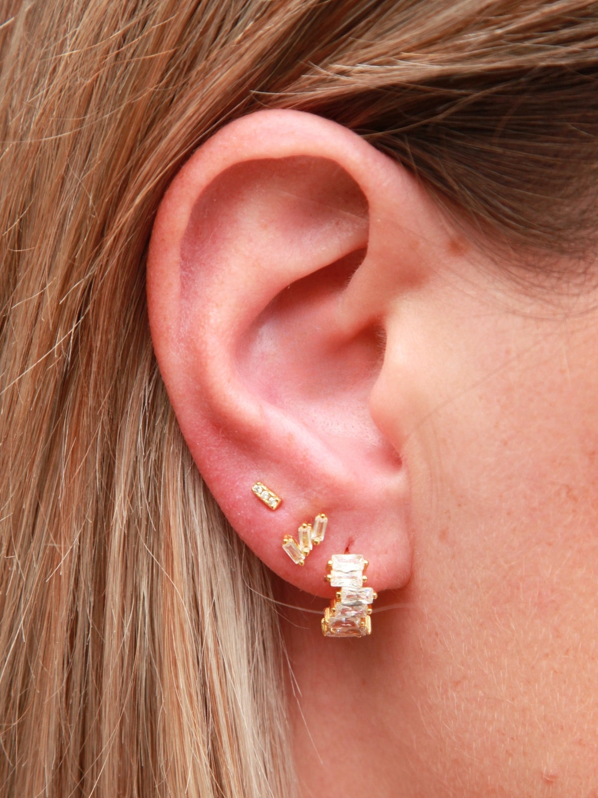 Close-up of an ear wearing gold earrings with a neutral background