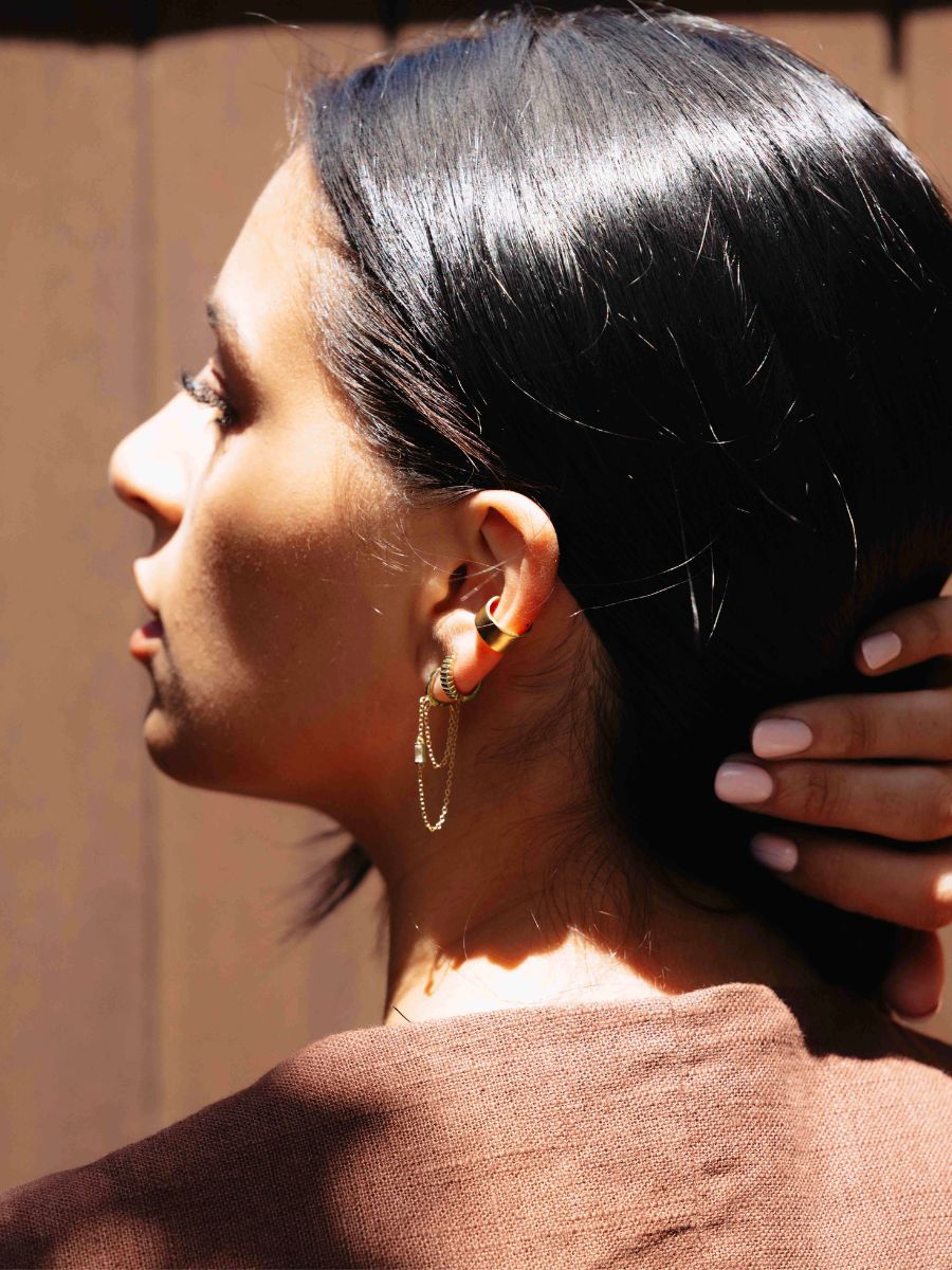 A woman wearing chain huggies with brown background