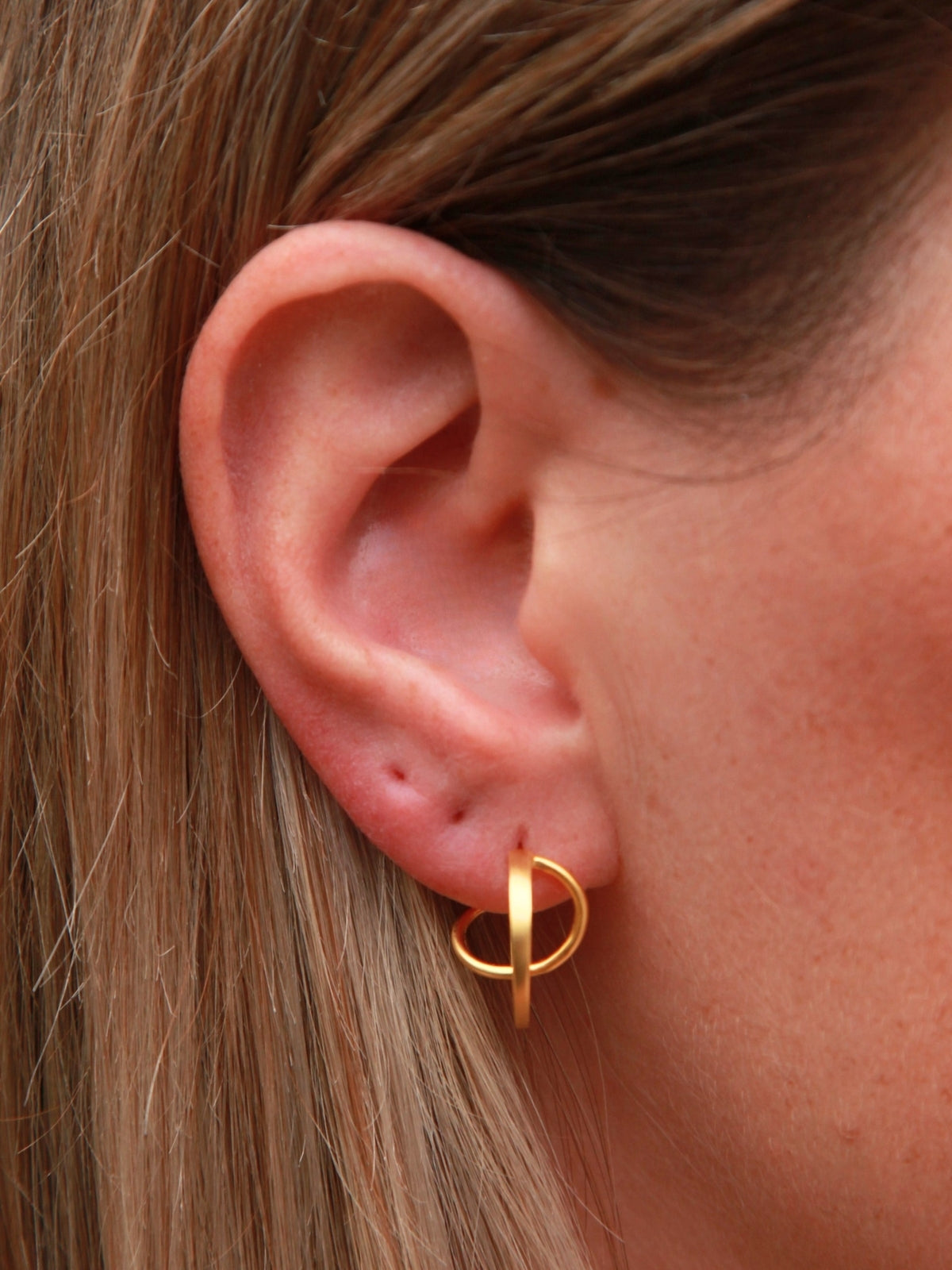 Gold hoop earring worn by a person with blonde hair.