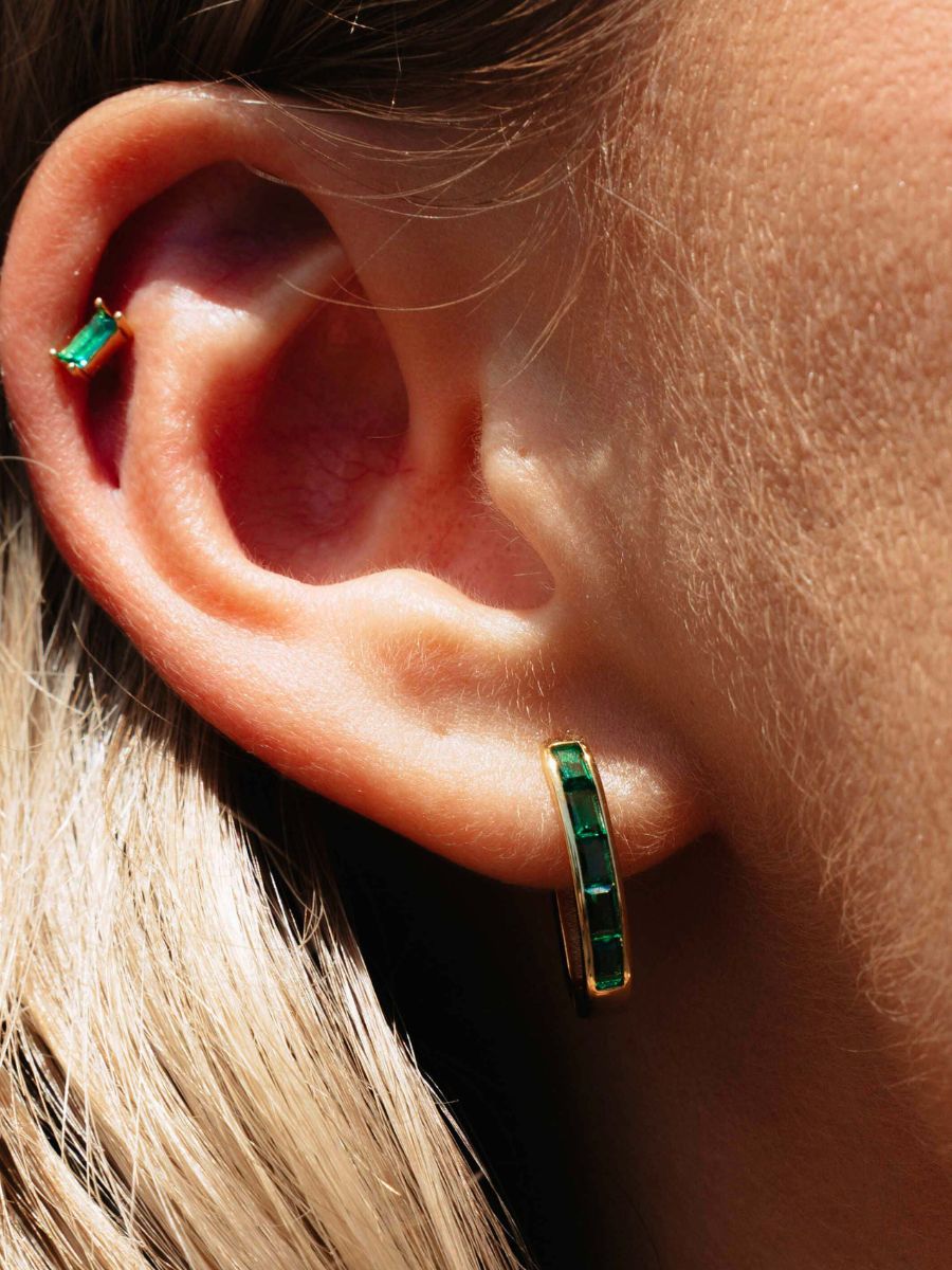 Close-up of an ear wearing green and gold hoop earrings.