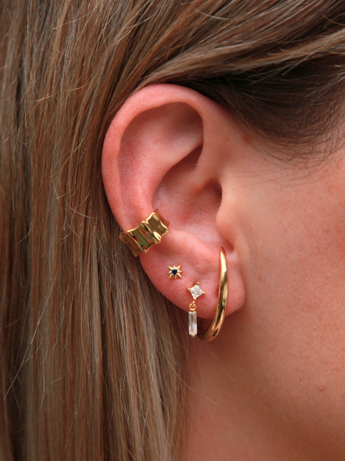 Close-up of an ear wearing gold hoop earrings with small gemstones.