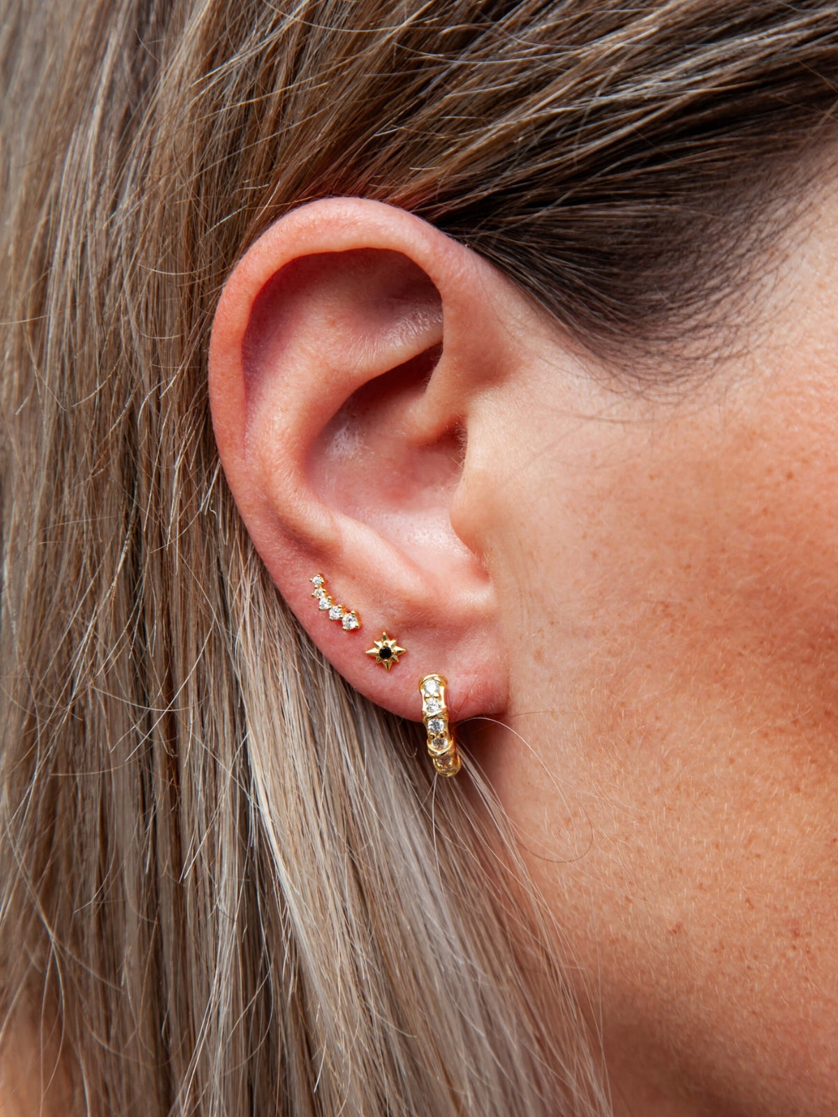 Close-up of an ear wearing gold hoop earrings with small gemstones.