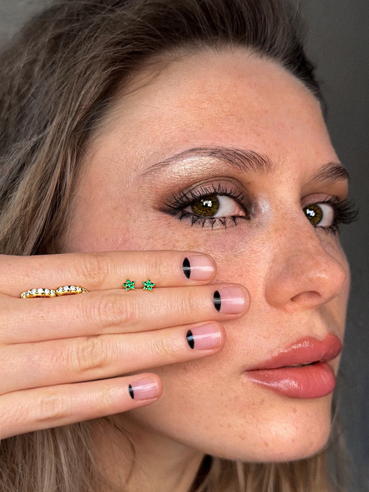 close up shot of a woman holding two pairs of earrings in her hand against her face