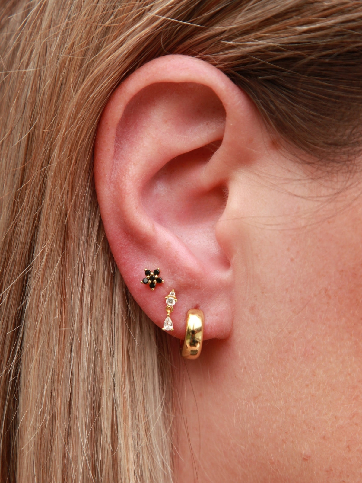 Close-up of an ear with gold hoop earrings and a small stud earring.