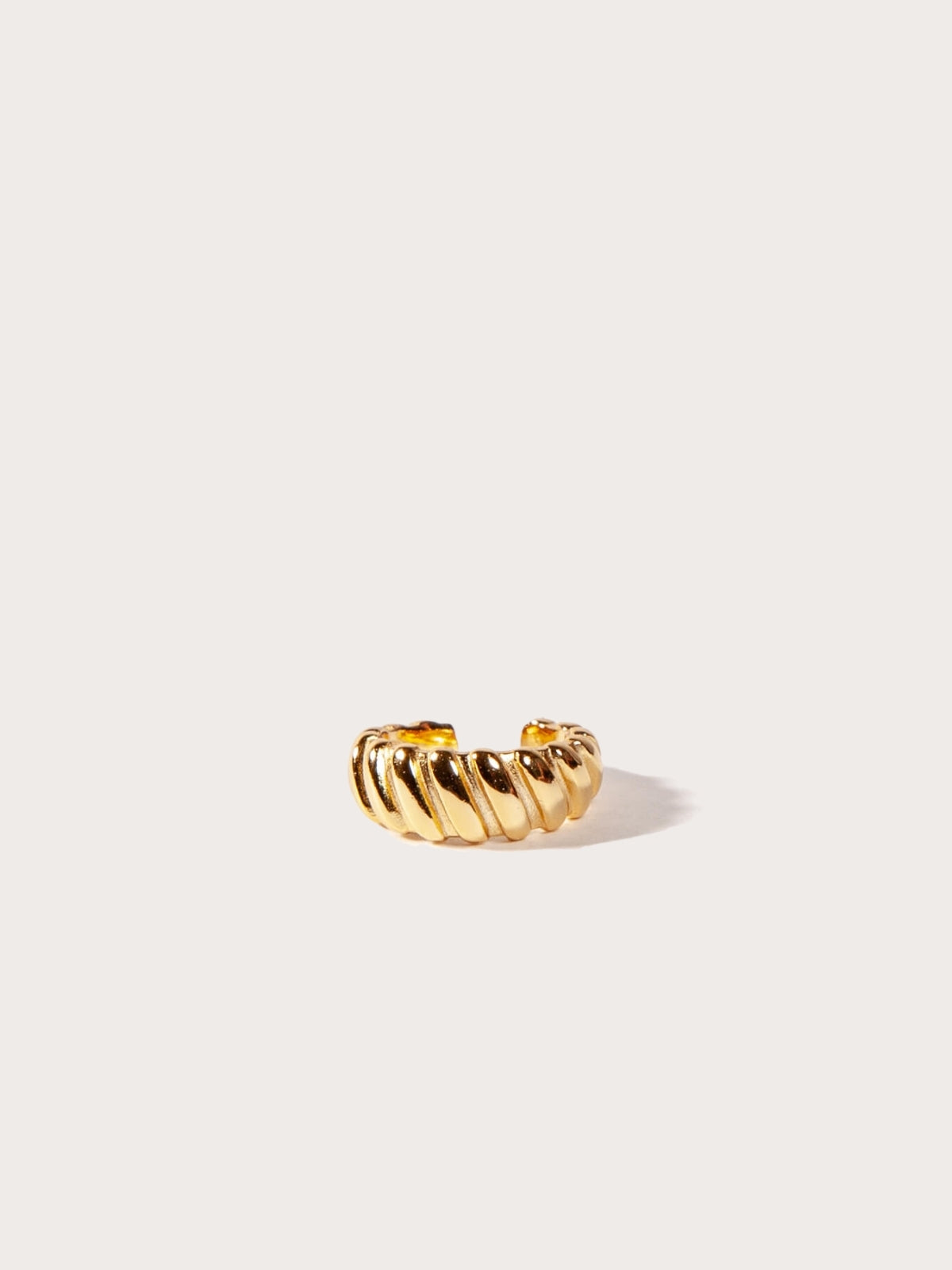 Gold croissant cuff earring on a light beige background
