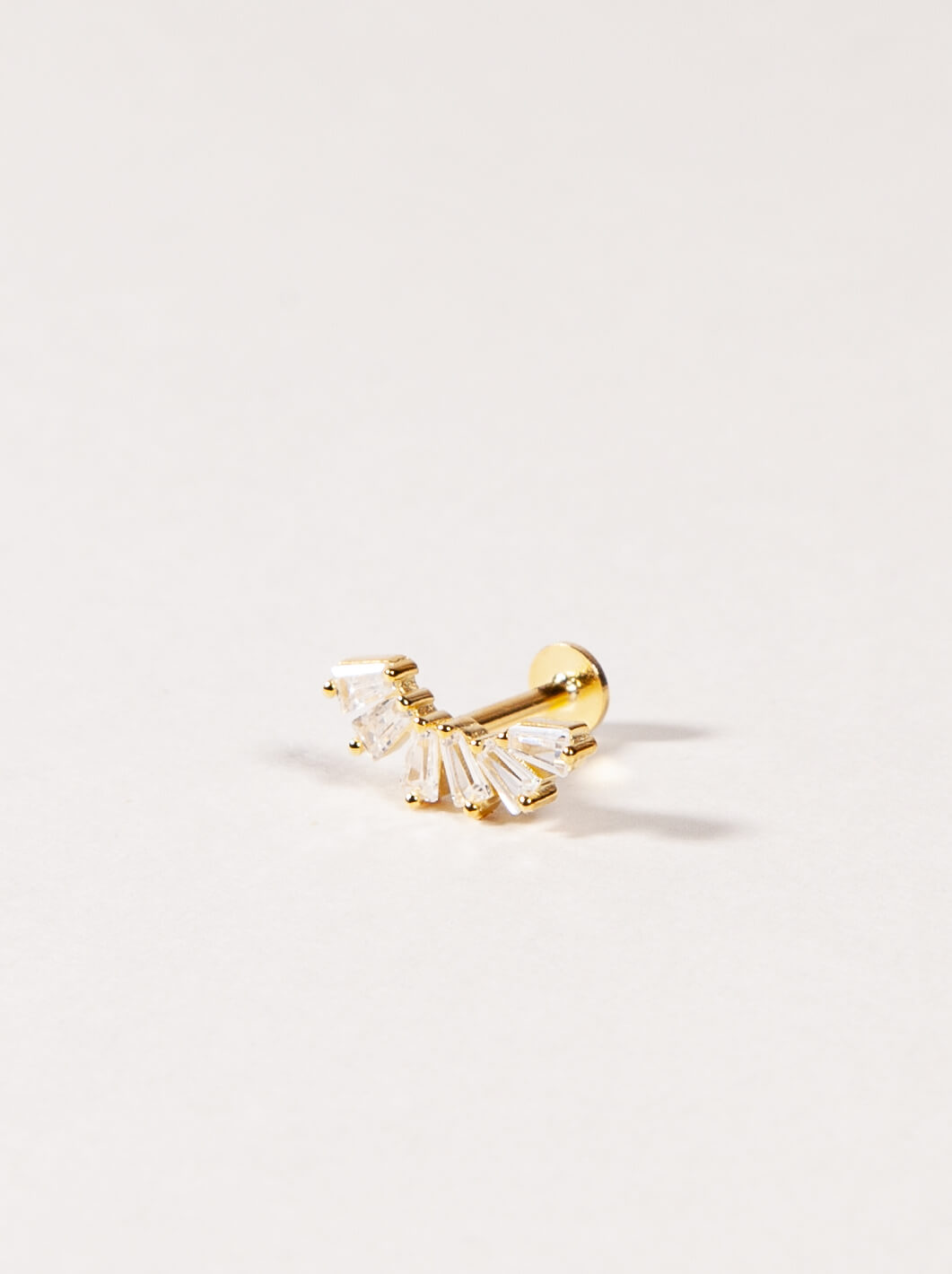 A gold crown-like shape with baguette-cut stones stud earring on a light beige background