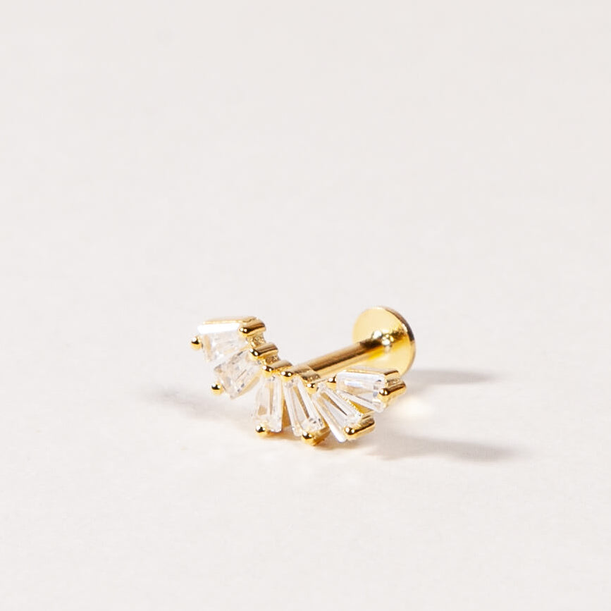 A gold crown-like shape with baguette-cut stones stud earring on a light beige background