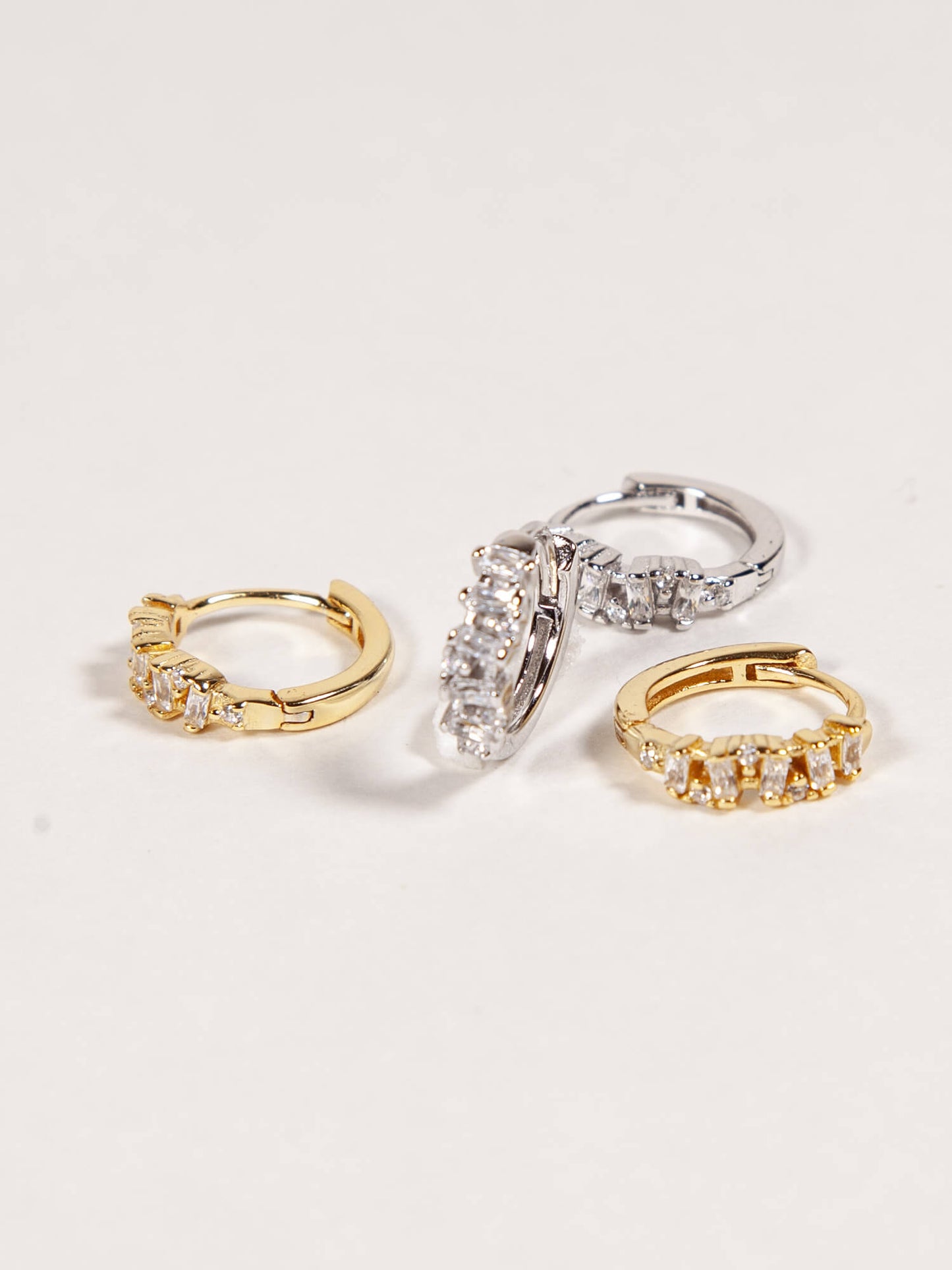 Gold and silver huggies with baguette CZ stones on a white background