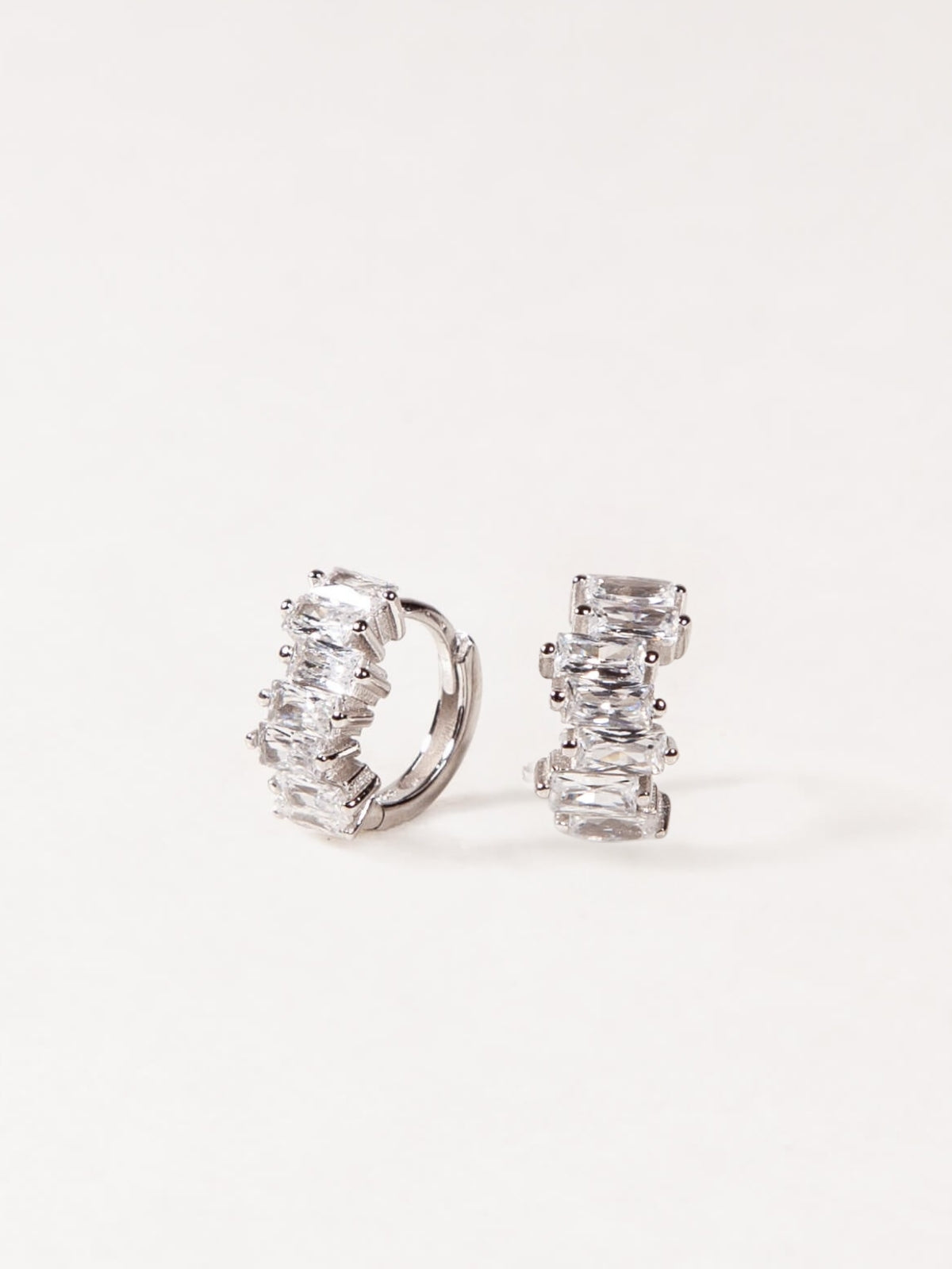 Pair of silver hoop earrings with clear gemstones on a white background