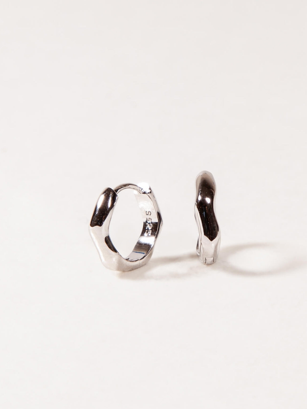 Silver modern wave huggies earrings on a white background
