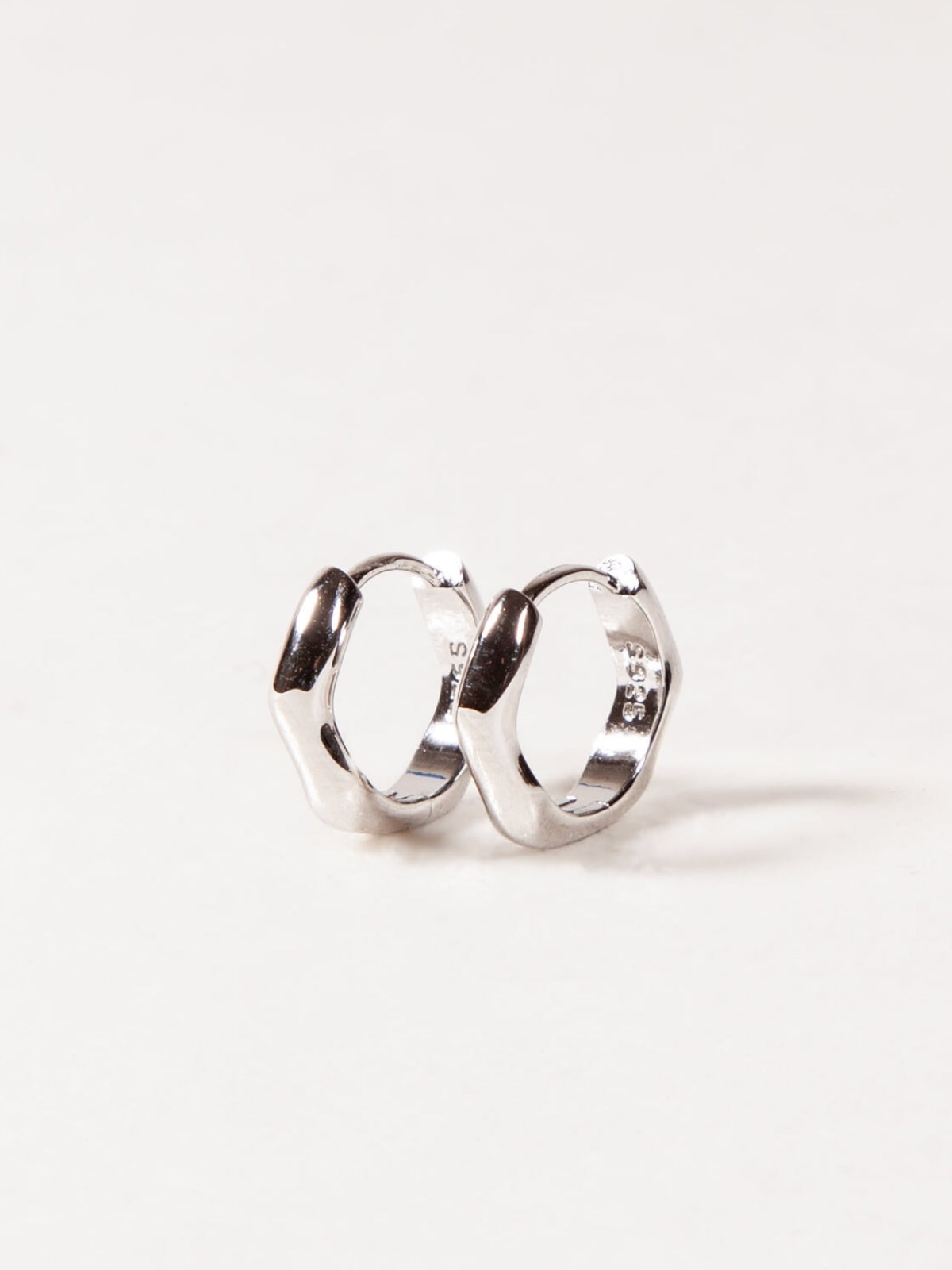 silver modern wave huggies earrings on a white background