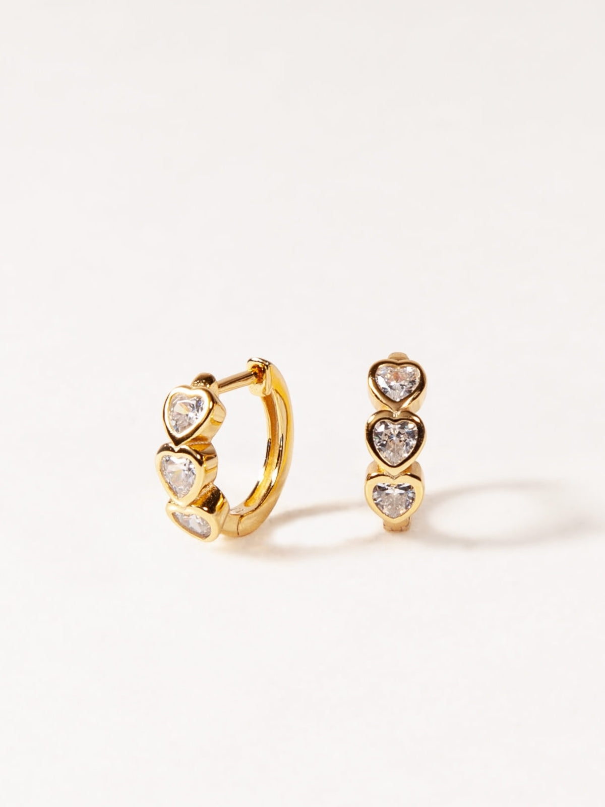 Gold hoop earrings with heart-shaped gemstones on a white background
