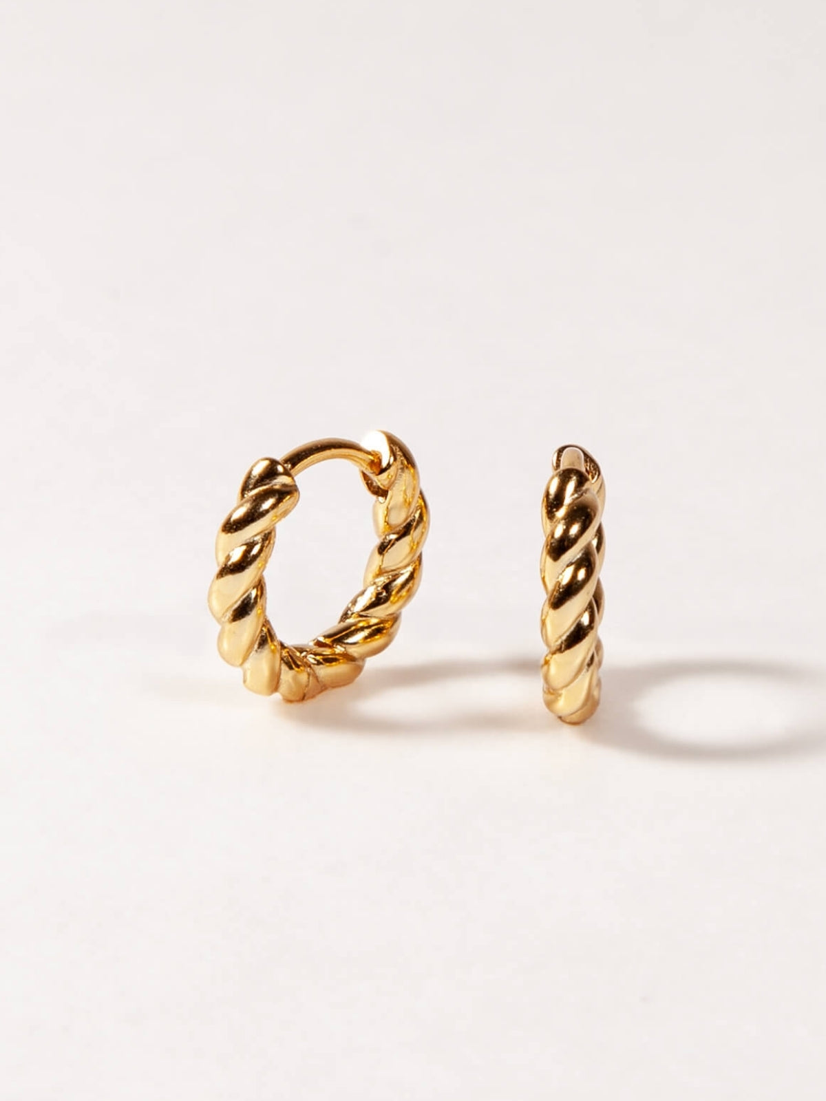 Pair of gold twisted hoop earrings on a white background