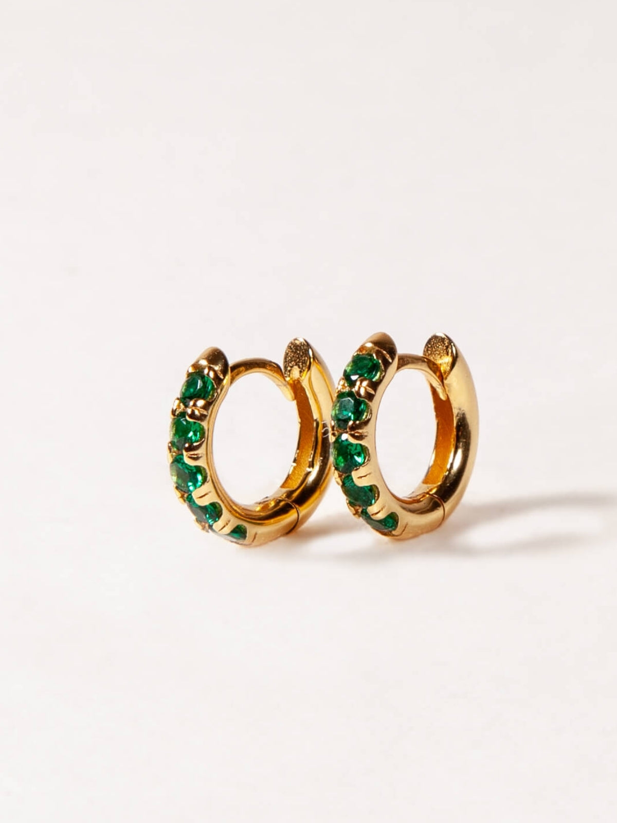 Gold hoop earrings with green gemstones on a white background