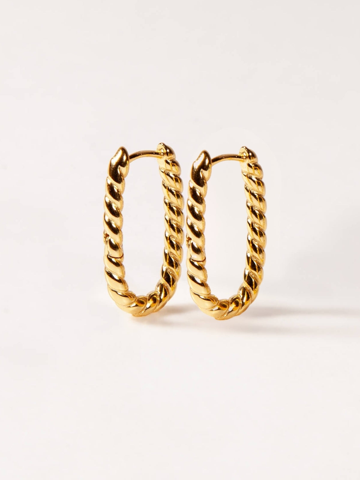 Pair of gold twisted U hoop earrings on a white background