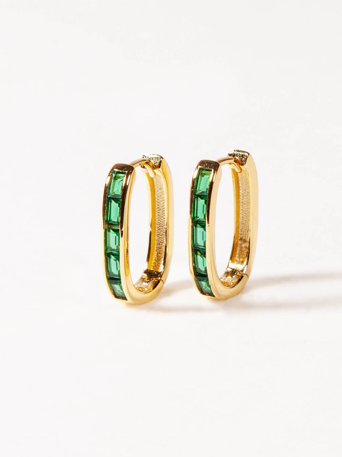 Gold U shaped hoop earrings with green gemstones on a white background