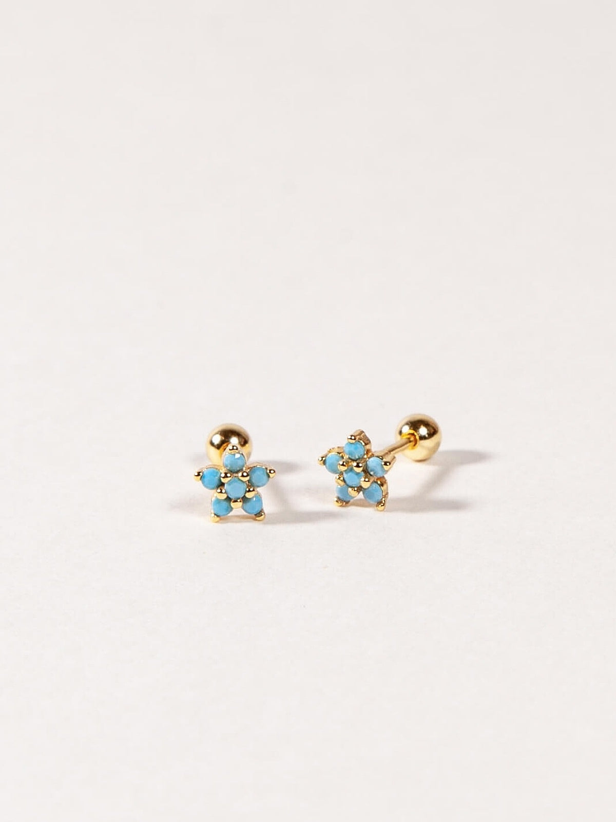 Pair of gold flower-shaped earrings with  turquoise blue gemstones on a white background