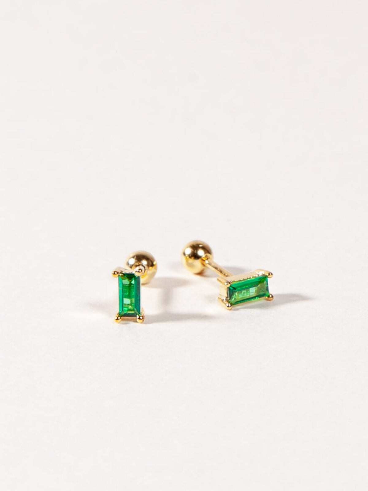 Gold baguette earrings with green CZ stones on a white background