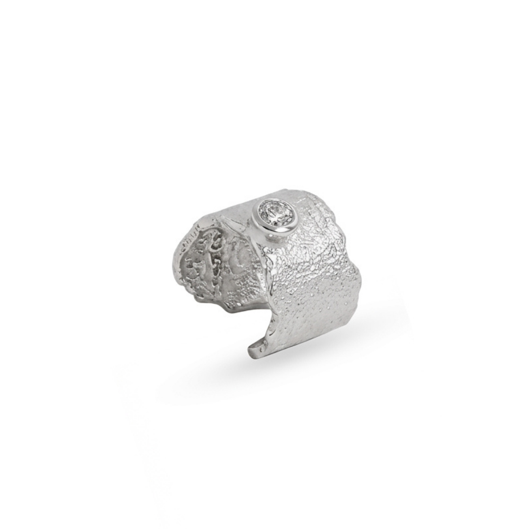 A textured silver cuff, featuring a small clear gemstone set into the top, photographed on a clean white background.
