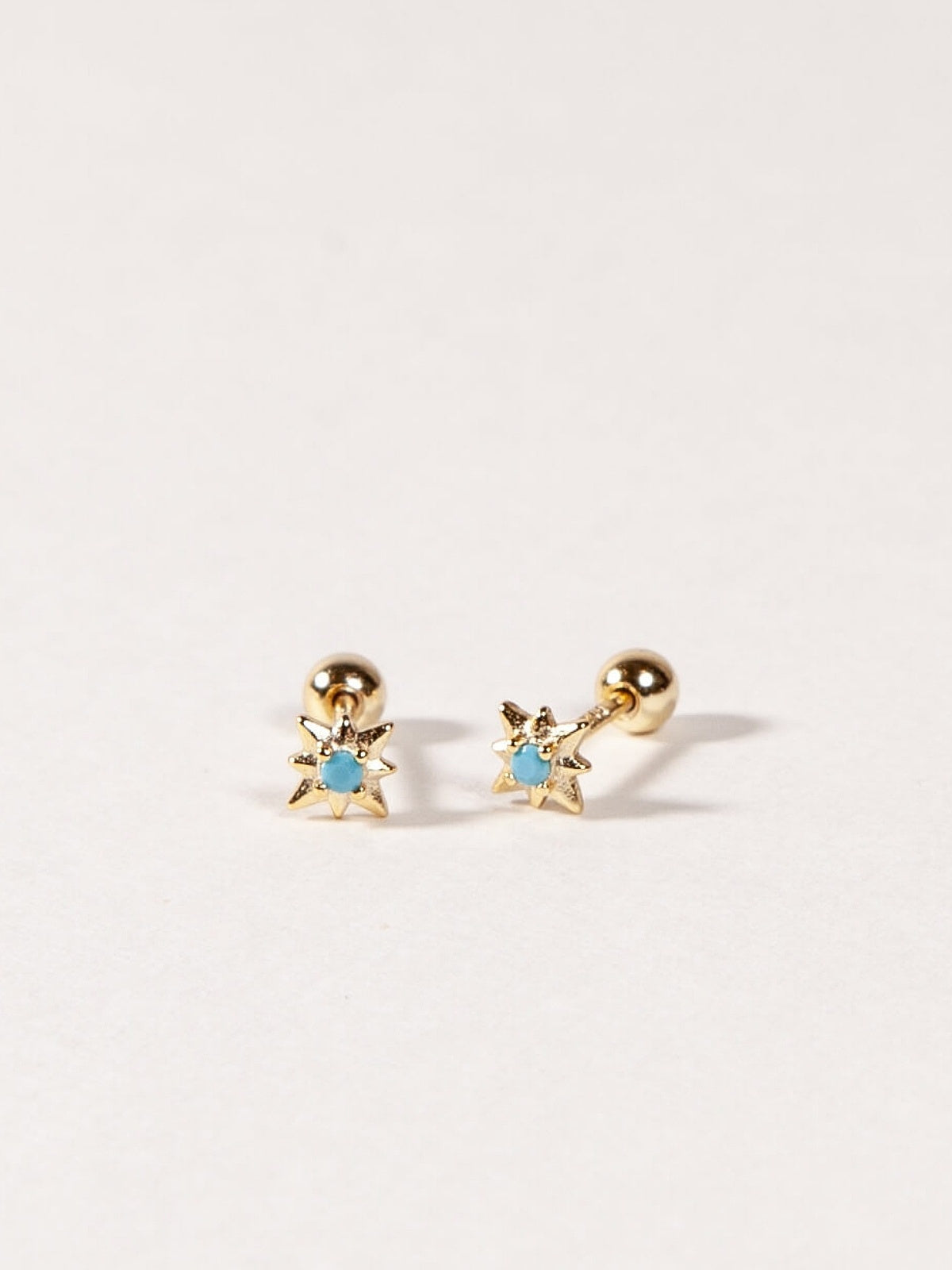 Pair of gold star shape earrings with turquoise blue CZ Stones on a light gray background