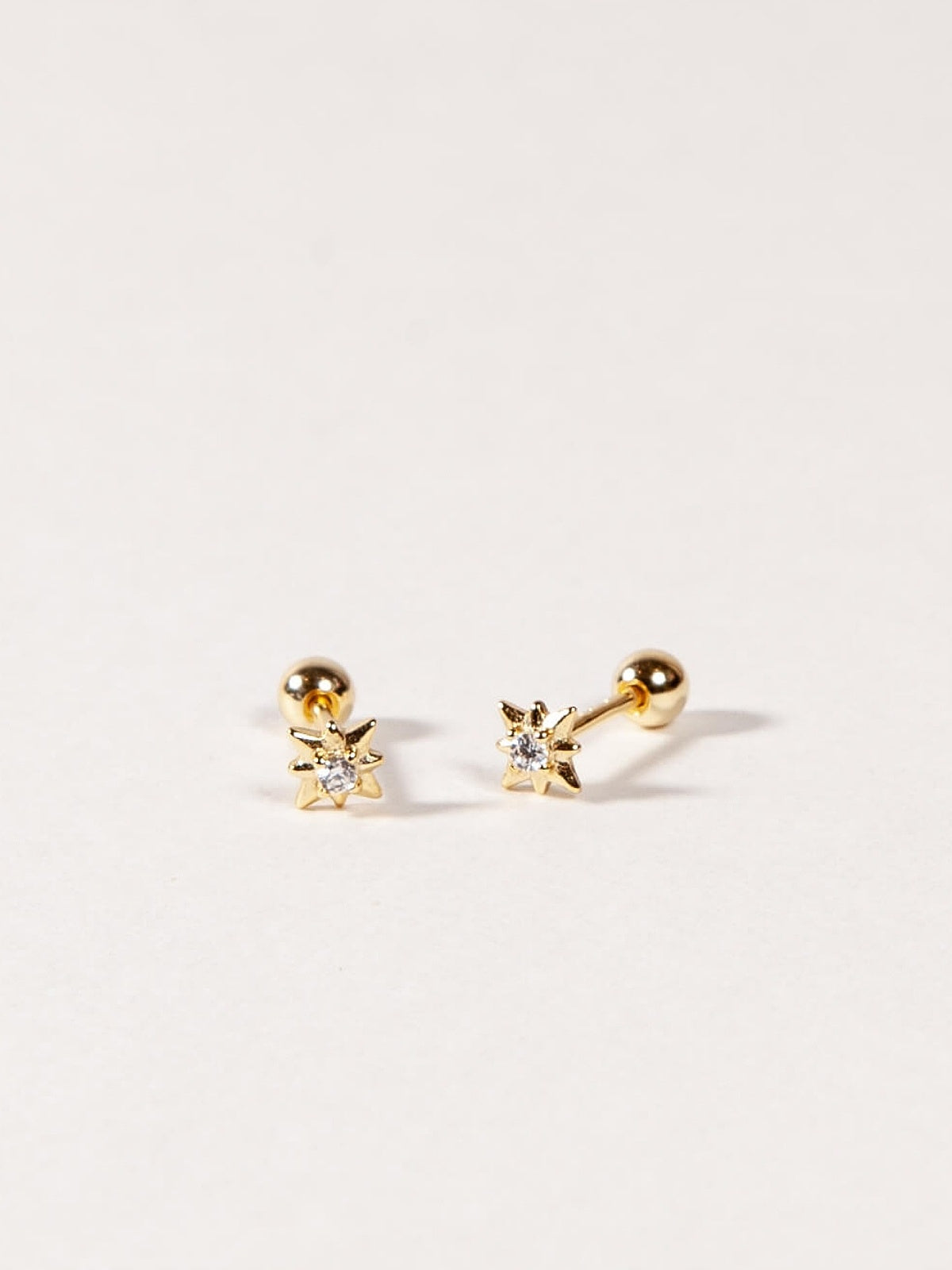 Pair of gold star shape earrings with diamond color  CZ Stones on a light gray background