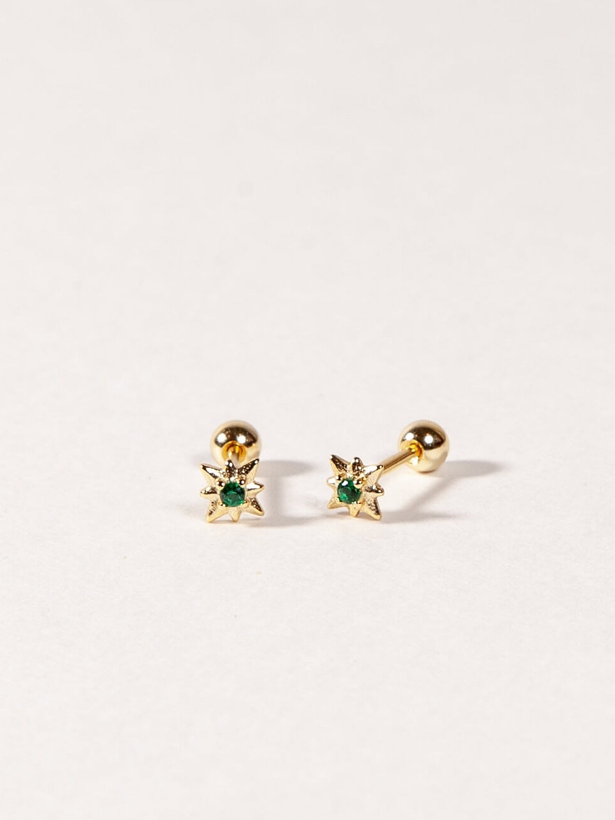 Pair of gold star shape earrings with emerald green CZ Stones on a light gray background